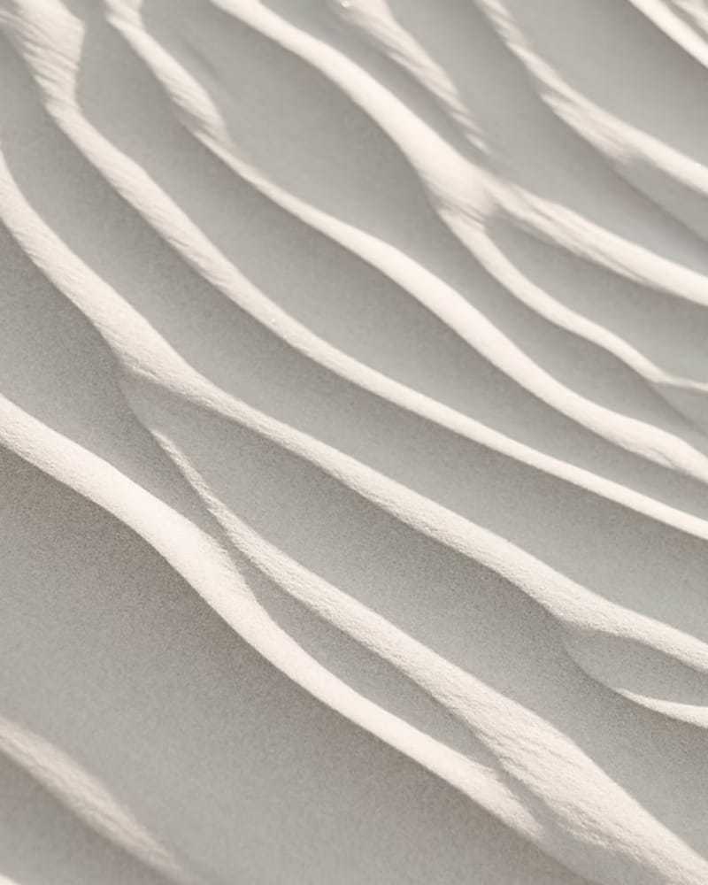 Ripples in white sand under soft sunlight, creating a serene and tranquil pattern.