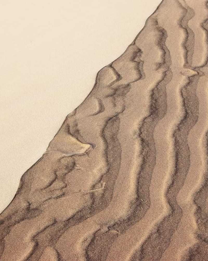 Wavy sand patterns with contrasting light and dark shades on a dune surface.