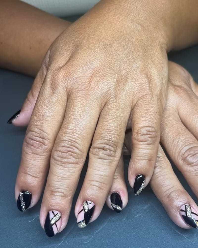 Nail art with black and silver geometric designs on a person's fingernails.