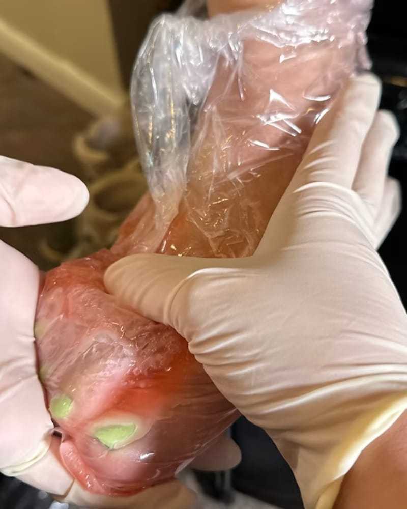 Gloved hands preparing meat in a clear plastic wrap with green seasoning.